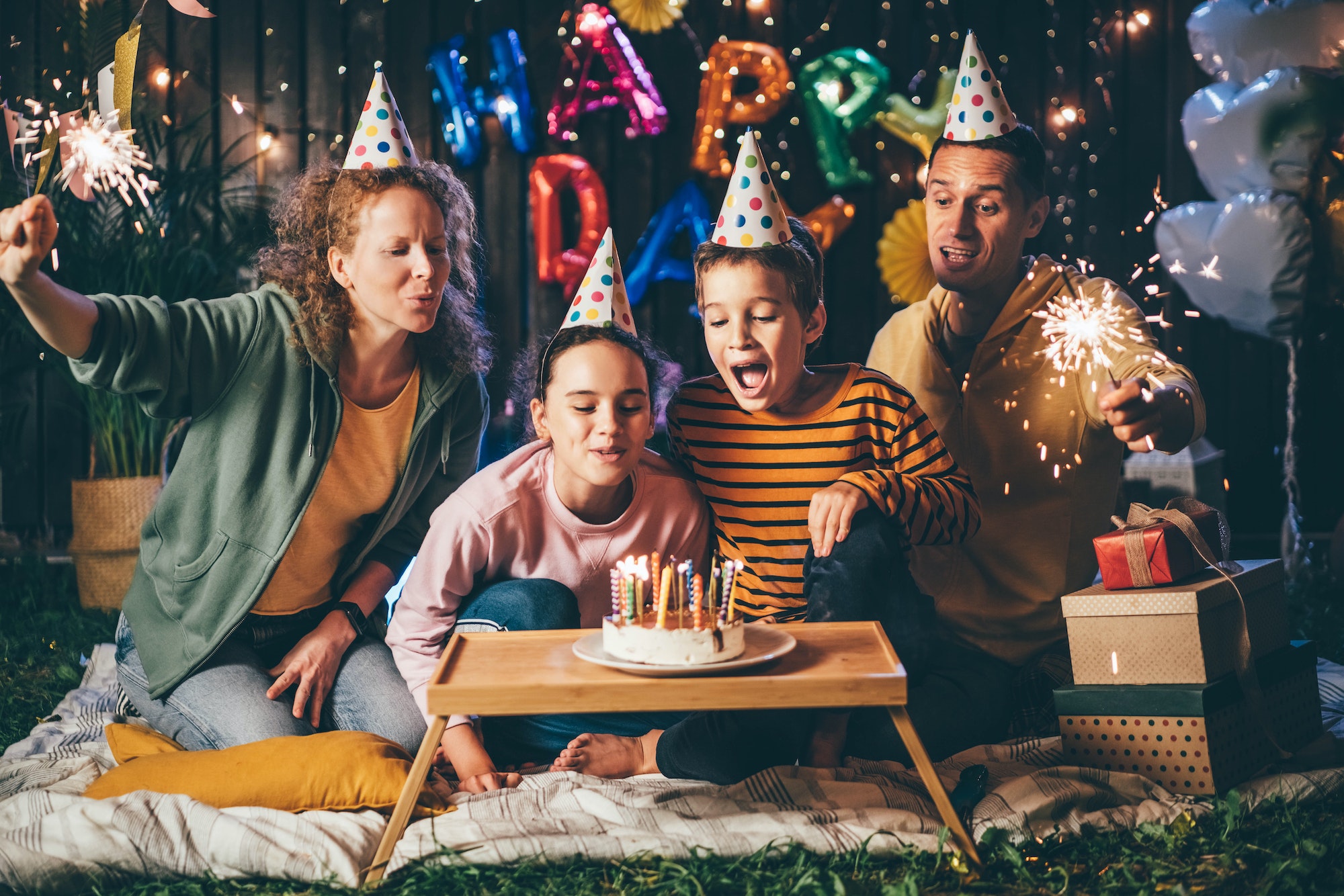 parents and children trying to blow burning candles on birthday cake celebrate