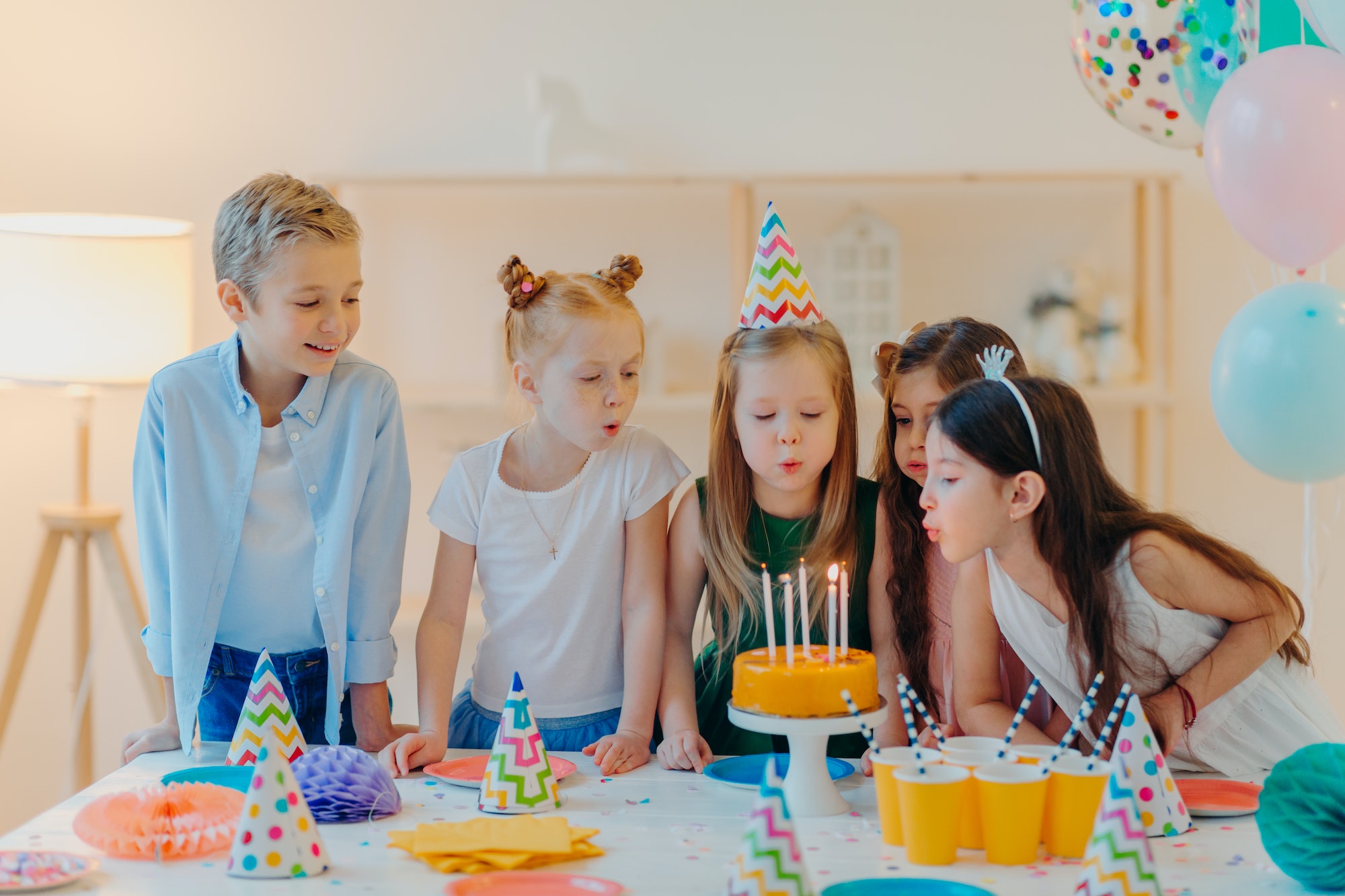 Small kids celebrate birthday party, blow candles on cake, gather at festive table
